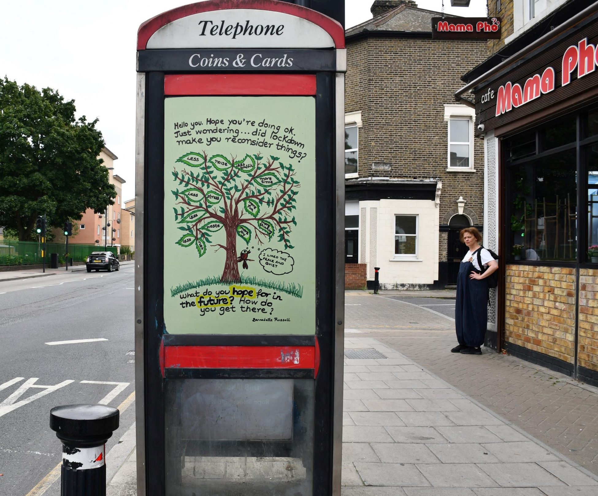 Photo of a public phone box on a street outside a restaurant. The top pane of glass on the door has a poster on it with the text 