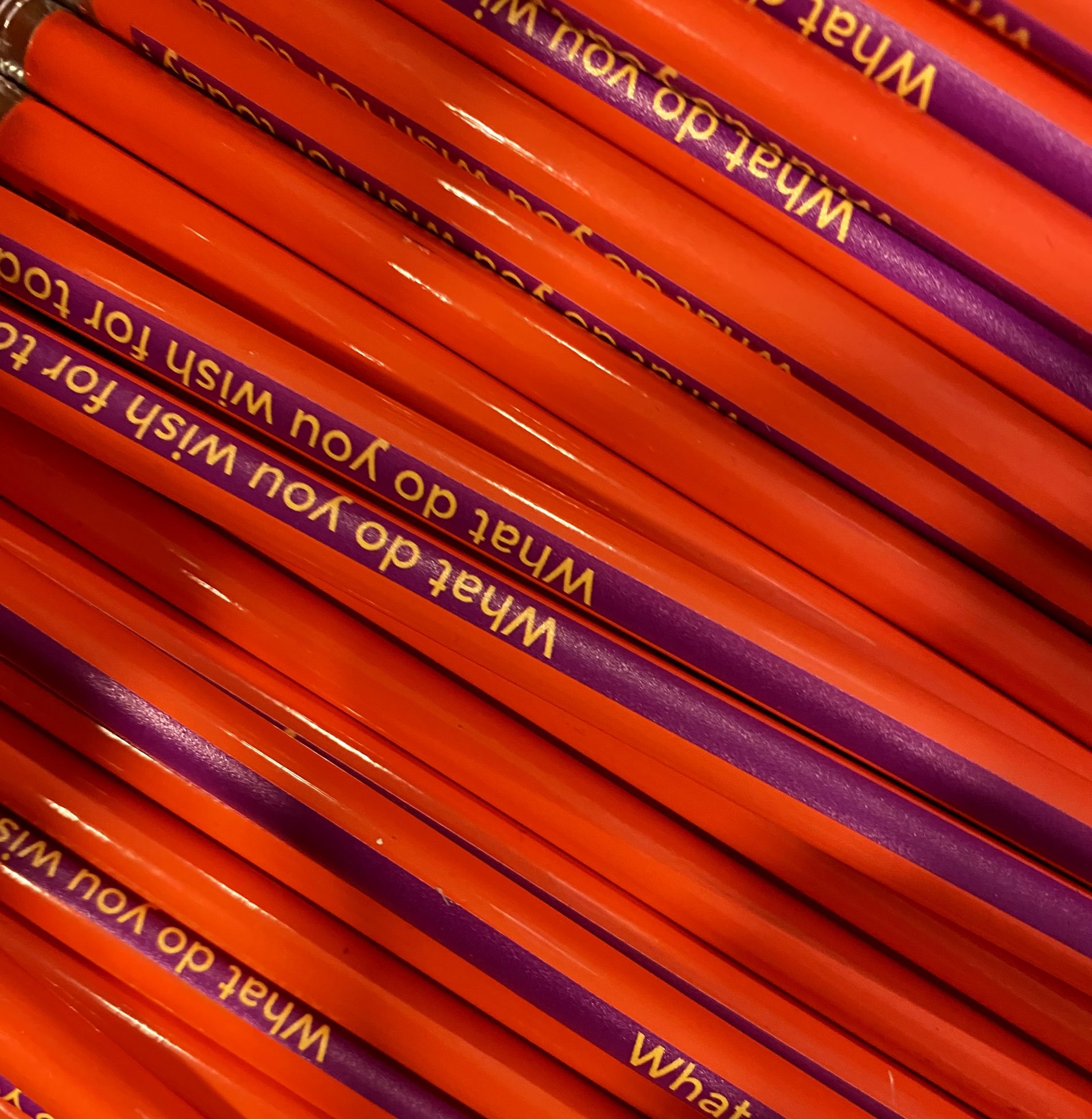 A close up photo of a box of orange pencils. Each pencil has a purple stripe along it with the text 