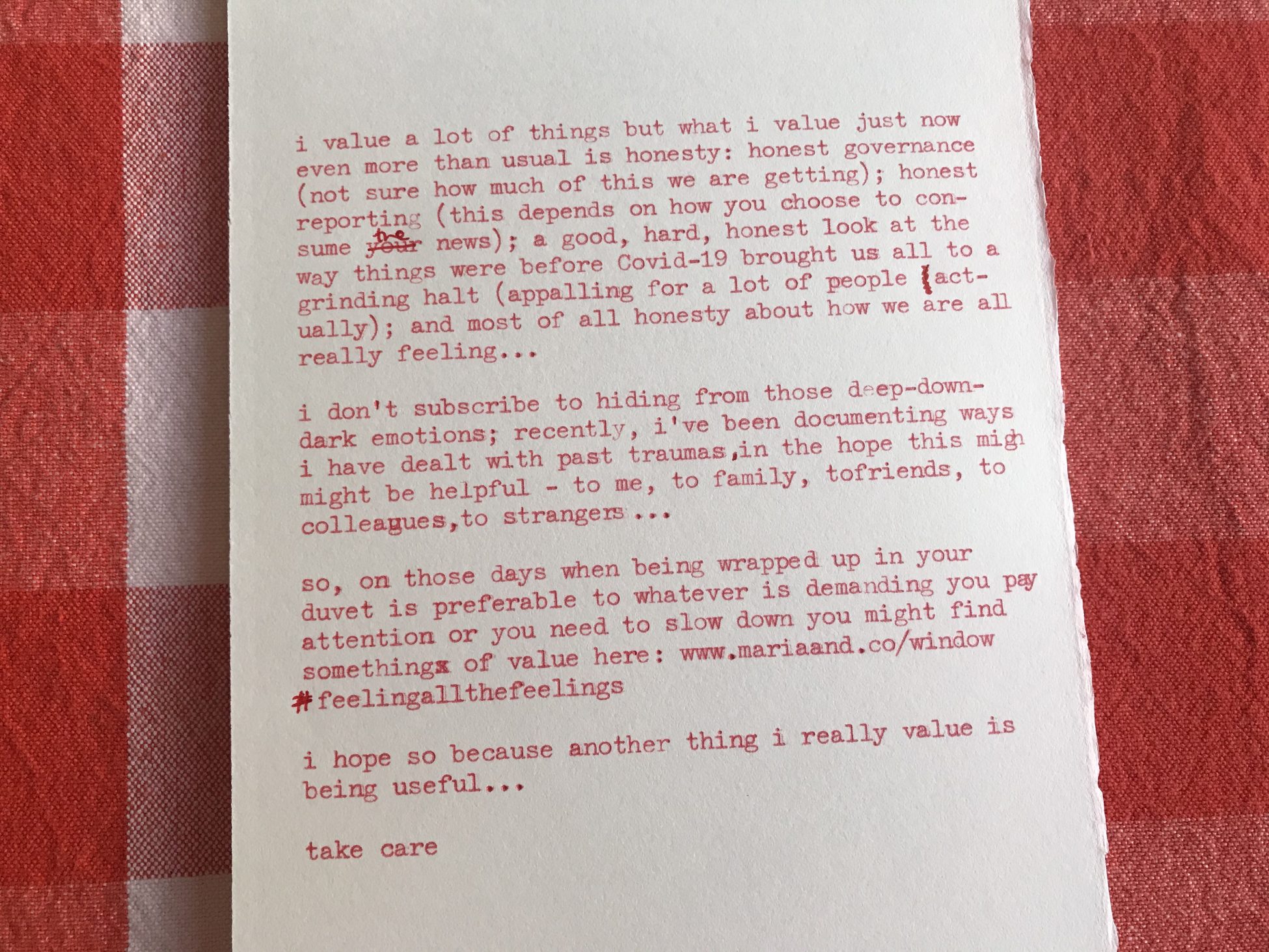 Blog piece which has been typed in red ink on a typewriter and corrected by hand in red pen, the paper is lying on a red gingham cloth. A transcription is provided below this image.