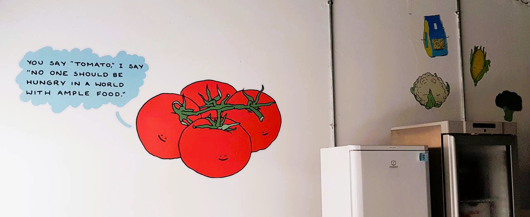 Photo of a vinyl decal on a wall, a group of four anthropomorphised tomatoes connected by a vine. One is saying 